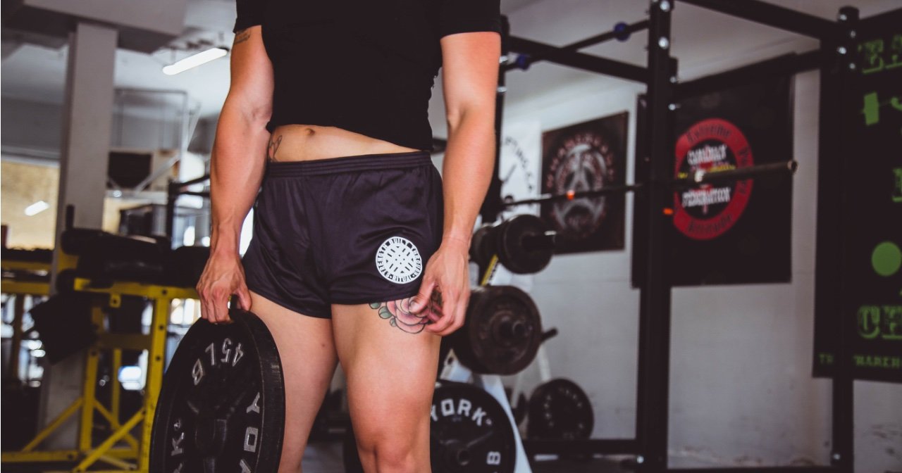 Woman holding 45 lb plate in front of squat rack
