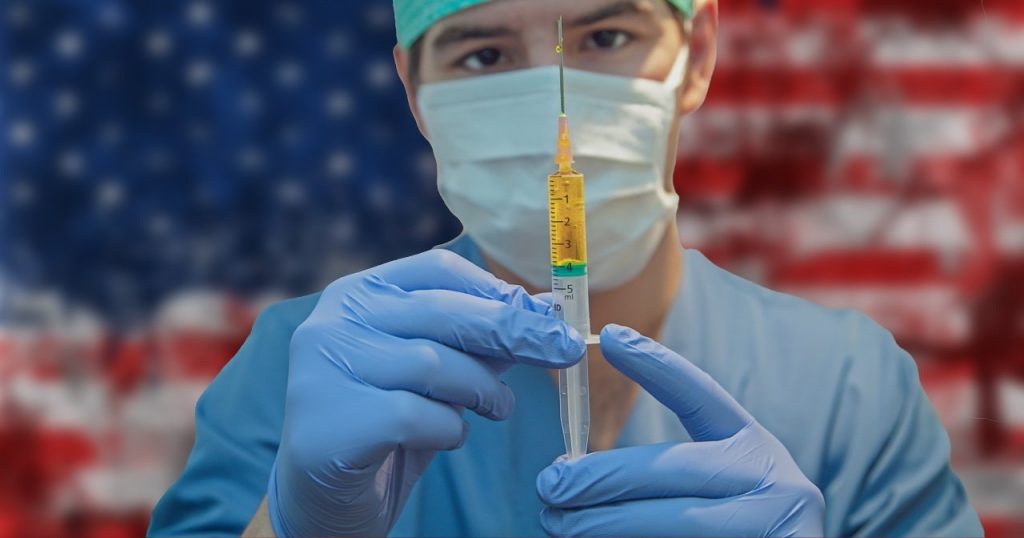 Doctor in a mask holding a needle in front of the American flag