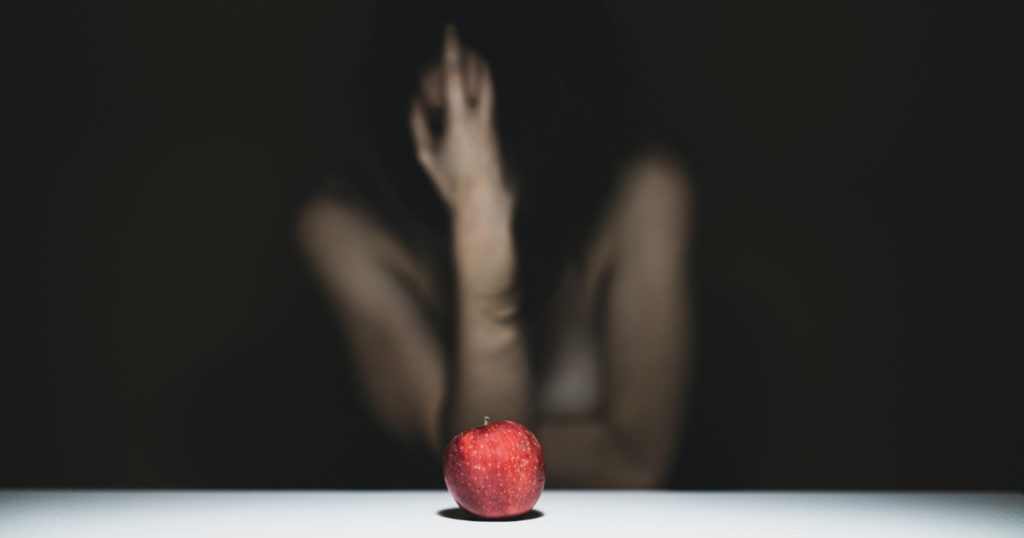 Woman holding her head in her hand in front of an apple on the table