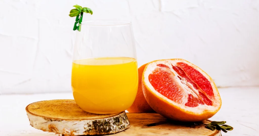 Glass of orange juice with slice of grapefruit alongside it